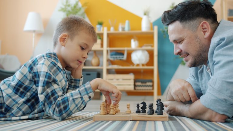 Father and son playing chess on the floor.