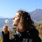 Donna allìaperto in primavera mentre soffia un soffione, simbolo delle allergie stagionali e del contatto con il polline