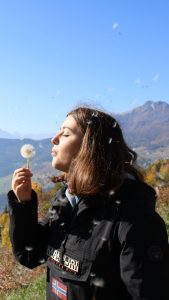 Donna allìaperto in primavera mentre soffia un soffione, simbolo delle allergie stagionali e del contatto con il polline