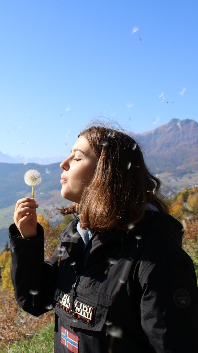 Donna allìaperto in primavera mentre soffia un soffione, simbolo delle allergie stagionali e del contatto con il polline