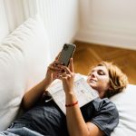 Donna con un libro che guarda lo smartphone invece di leggere.