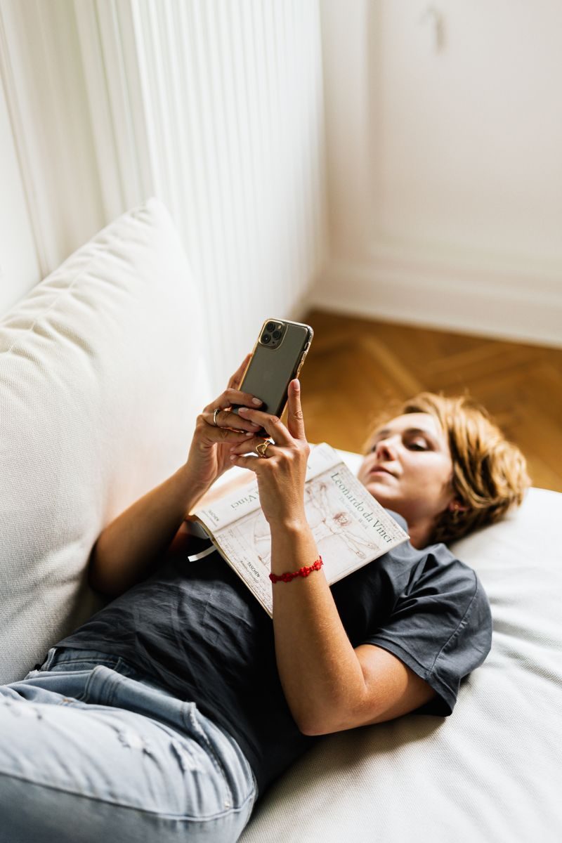 Donna con un libro che guarda lo smartphone invece di leggere.