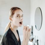 Donna che si lava denti davanti allo specchio del bagno