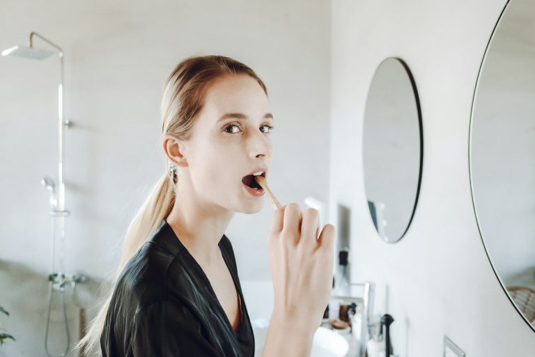 Donna che si lava denti davanti allo specchio del bagno
